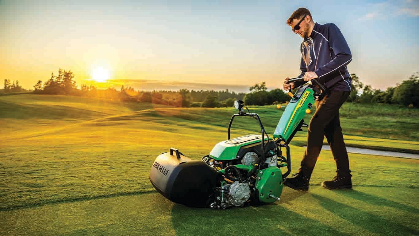 man pushing an electric walking greens mower at sunrise
